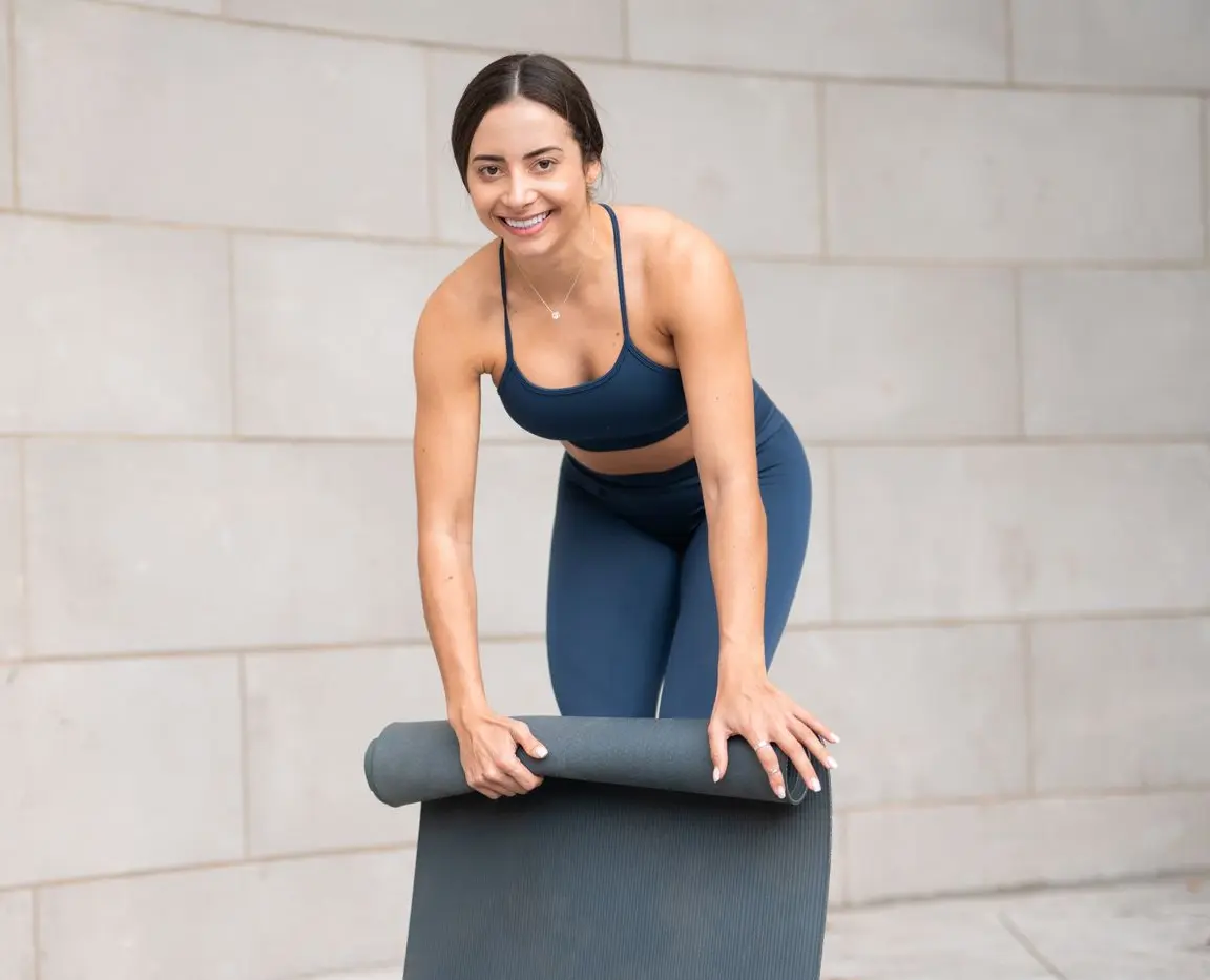 Hayane rolling a yoga mat and smiling.