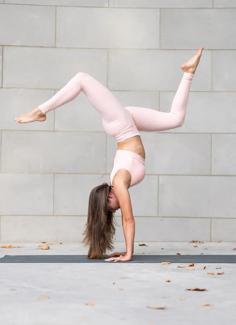 Hayane doing an upside-down yoga pose in front of a stone wall outside.