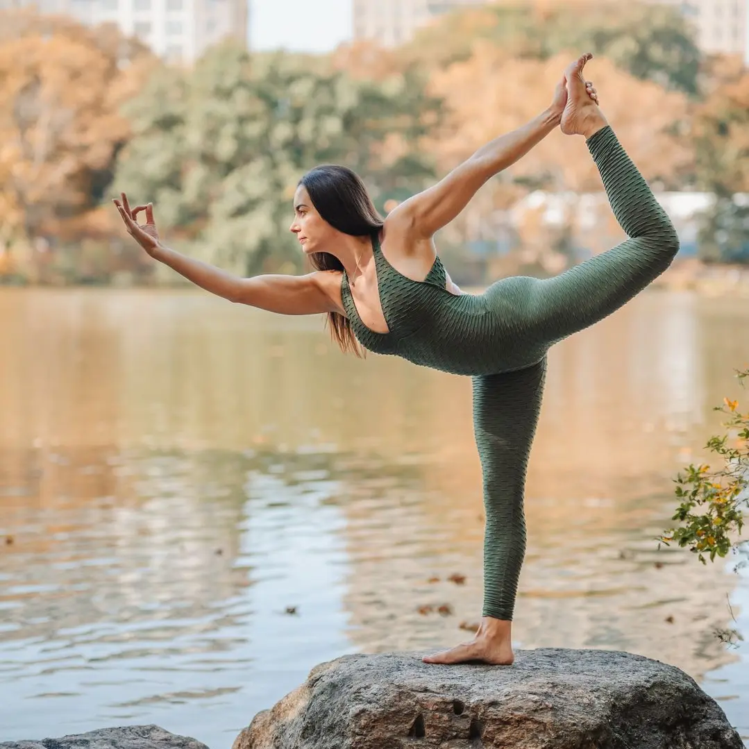 Hayane balancing in a one-legged yoga pose outside on a rock in front of water.