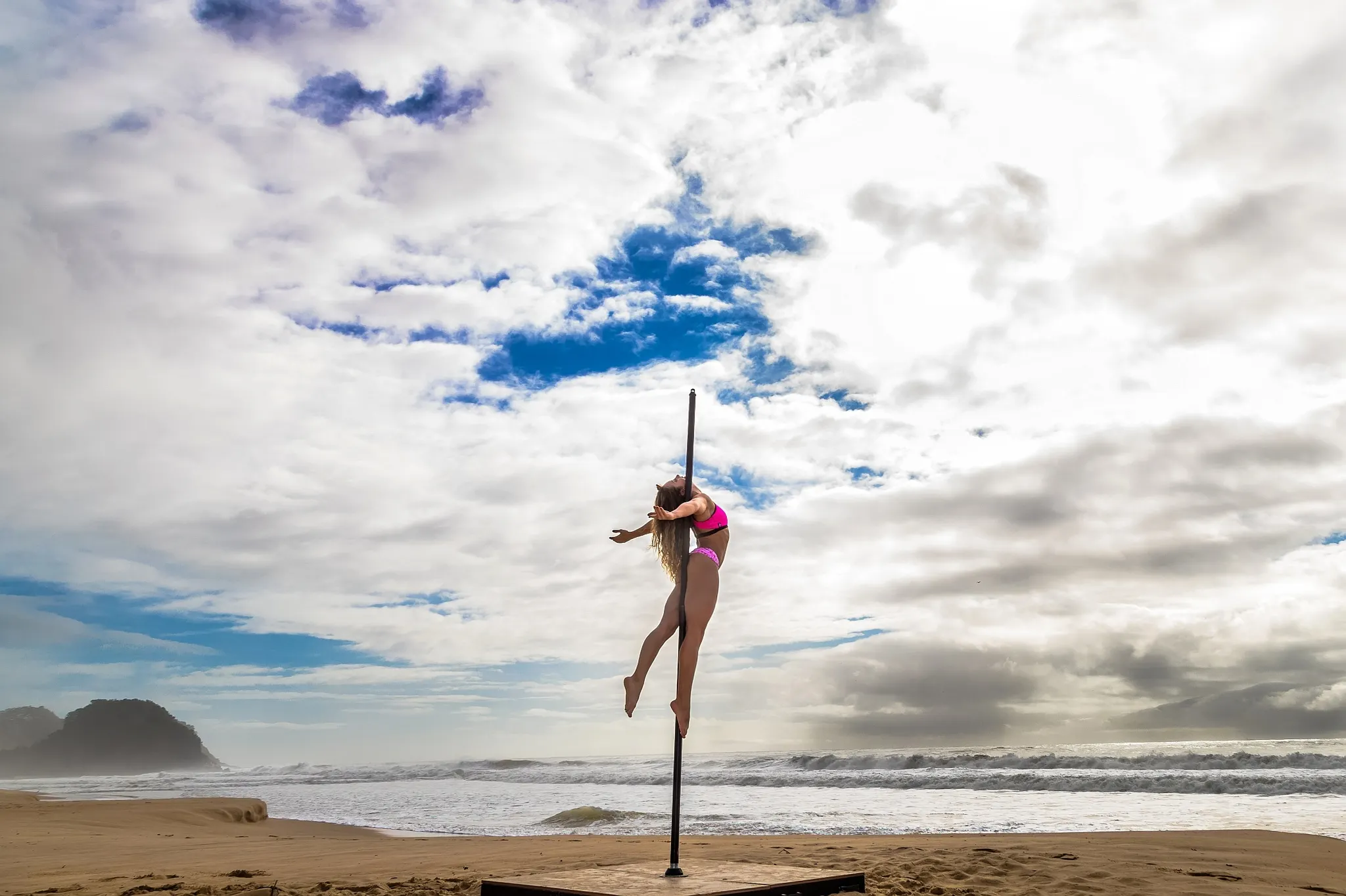 Hayane posing on a pole in the air, outside at a beach.