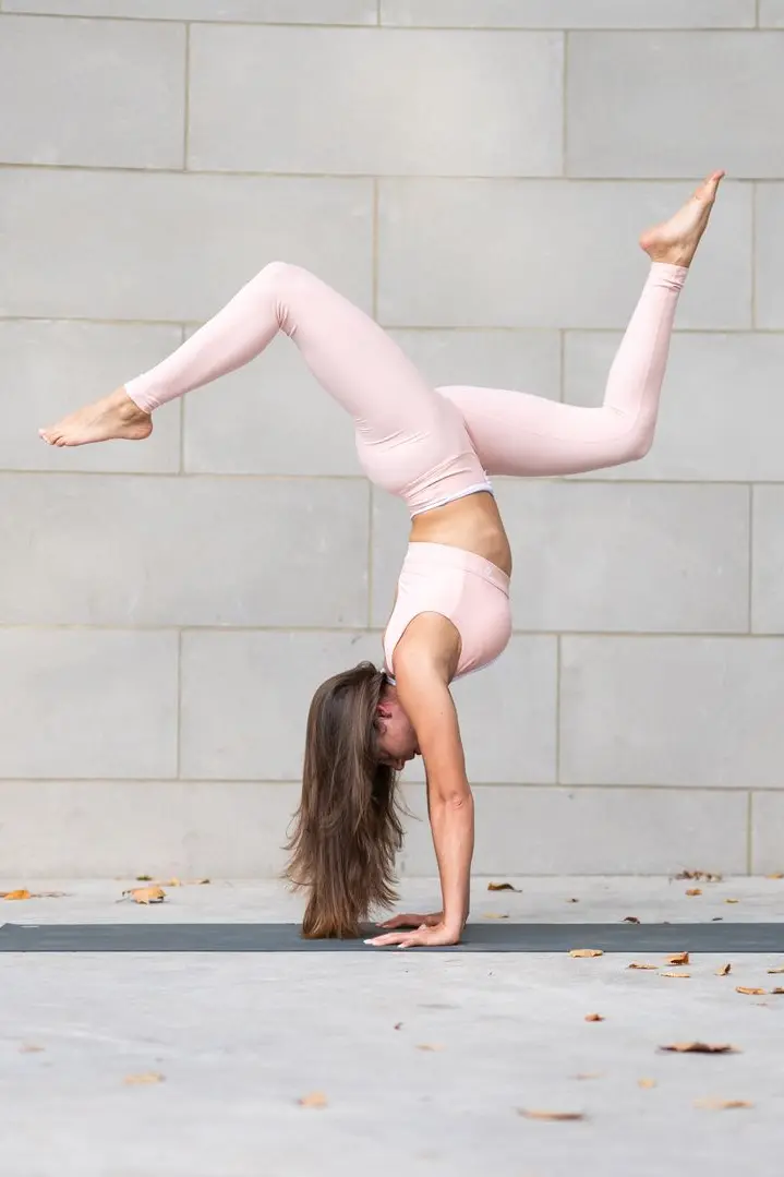 Hayane doing an upside-down yoga pose in front of a stone wall outside.